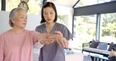 Kıdemli Asyalı kadına kol egzersizlerinde yardım etmek, evde bakım terapisi sağlayan fizyoterapist. Fizyoterapi, rehabilitasyon, sağlık hizmetleri, bakıcı, hareketlilik, sağlık