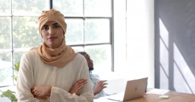 Ofiste kolları bağlı gülümseyen bir kadın, arkasında dizüstü bilgisayarla çalışan bir iş arkadaşı. İş, işyeri, profesyonel, takım çalışması, üretkenlik, işbirliği