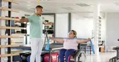 Rehabilitasyon, direniş bantları kullanan terapist tekerlekli sandalyedeki felçli kadına yardım ediyor. fizyoterapi, egzersiz, sağlık, yardım, hareketlilik, destek, değiştirilmemiş, yavaş çekim