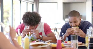 Çeşitli arkadaşlar hamburger yer ve birlikte yemek masasında öğle yemeğinin tadını çıkarırlar. yemek, eğlence, toplanma, yemek