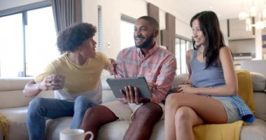 Evde, çeşitli arkadaşlar takılıyor, tablet kullanıyor ve kanepede otururken kutlama yapıyorlar. Arkadaşlık, teknoloji, kutlama, eğlence, eğlence, dijital aygıtlar