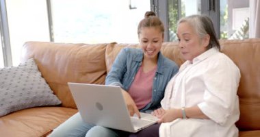 Dizüstü bilgisayar kullanan, Asyalı genç bir kadın evdeki kanepede yaşlı Asyalı kadınlara öğretmenlik yapıyor. Teknoloji, akıl hocalığı, nesiller arası eğitim, öğrenme, bağlanma, eğitim