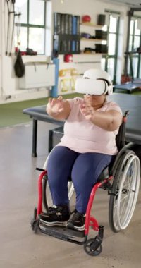 Dikey video: VR kulaklık kullanan tekerlekli sandalyedeki kadın rehabilitasyon merkezinde kol egzersizi yapıyor. Sanal, egzersiz, terapi, sağlık, teknoloji, engellilik, yavaş çekim