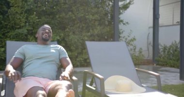 Arka bahçedeki şezlongda dinlenen, güneşli günün tadını çıkaran bir adam. Rahatlama, rahatlama, güneş ışığı, rahatlık, yaz, dinlenme