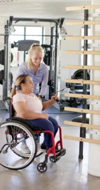 Dikey video: Terapistle egzersiz yapmak, tekerlekli sandalyeli bir kadının rehabilitasyon için spor aletlerini kullanması. Fizyoterapi, sağlık, terapi, fitness, egzersiz, sakatlık, ağır çekim