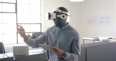 Modern ofis ortamında tablet üzerinde çalışan bir adam, VR kulaklığı kullanıyor. Teknoloji, sanal gerçeklik, yenilik, uzaktan çalışma, iş, dijital