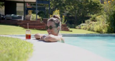 Havuzda dinlenen, güneş gözlüğü takan, güneşli bir günde içki içen bir kadın. Havuz kenarı, rahatlama, güneş ışığı, boş zaman, tatil, keyif