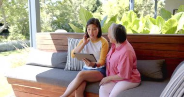 Yaşlı Asyalı kadına tablet gösteriliyor. Kanepede oturan genç Asyalı kadına. Teknoloji, kıdemli, aile, öğretim, iletişim, nesiller arası