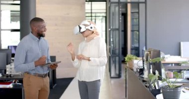 VR kulaklığı kullanan bir kadın, meslektaşı ile iş yerinde tablet tutarken projeyi tartışıyor. Teknoloji, işbirliği, takım çalışması, yenilik, profesyonel, dijital