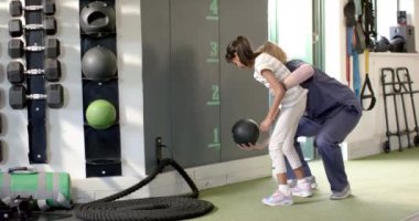 Serebral felçli bir kız rehabilitasyonda, terapist spor salonunda tıp topu egzersizinde yardımcı oluyor. fizyoterapi, sağlık, tedavi, terapi, destek, egzersiz, değiştirilmemiş, yavaş çekim