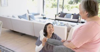 Fizyoterapist, oturma odasında bacak egzersizi yapan yaşlı Asyalı kadına yardım ediyor. rehabilitasyon, sağlık hizmetleri, yaşlılar, terapi, yardım, iyileşme