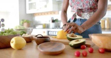 Afro-Amerikalı kadın evde mutfakta biber kesiyor. Koyu renk saçları var, çiçekli bluzu var, yemek hazırlıyor, değişmemiş, ağır çekimde.