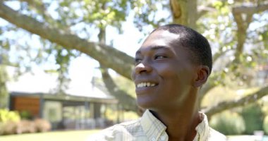 Genç bir Afrikalı Amerikalı erkek gülümsüyor, dışarı bakıyor, evde. Kısa siyah saçları, berrak bir teni var. Sıradan bir gömlek giyiyor. Değiştirilmemiş, ağır çekim.