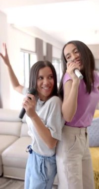 Dikey video: Karaoke söylemek, iki genç kızın evde mikrofonla takılmaktan hoşlanması. Gençler, arkadaşlar, eğlence, eğlence, müzik, gençlik