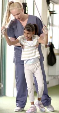 Dikey video: Engelli çocuğa destek olmak, rehabilitasyon sırasında terapist yardımı. terapi, sağlık, tıbbi, fizyoterapi, yardım, tedavi, yavaş çekim