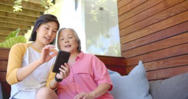 Akıllı telefon kullanarak, iki kadın kanepede oturup bir şeyleri tartışıyor. Teknoloji, iletişim, sohbet, ev, arkadaşlık, yaşam tarzı