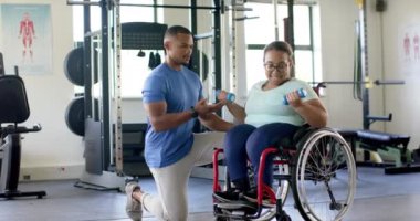 Tekerlekli sandalyedeki felçli kadına yardım etmek, spor salonunda yardımcı antrenör. Engellilik, spor, güç, eğitim, egzersiz, değişmemiş, ağır çekim