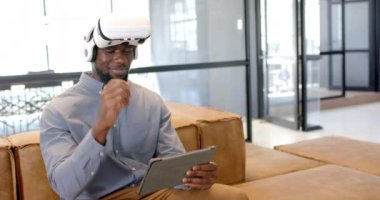 VR kulaklık kullanarak koltukta otururken elinde tablet tutan adam. Teknoloji, sanal gerçeklik, yenilik, modern, iş dünyası, dijital