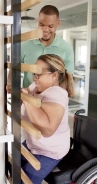 Dikey video: Terapistle egzersiz, tekerlekli sandalyedeki kadın rehabilitasyon için paralel barlar kullanıyor. Fizyoterapi, sağlık, egzersiz, hareketlilik, terapi, iyileşme, yavaş çekim