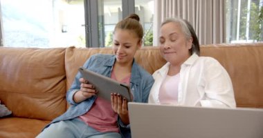 Tablet ve dizüstü bilgisayar kullanarak, Asyalı büyükanne ve torun evdeki kanepede kaynaşıyor. Aile, teknoloji, birliktelik, yaşlılık, çocuk, oturma odası