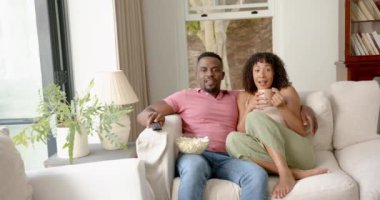 Kanepede dinlenen, gülen ve patlamış mısır ve kahvenin tadını çıkaran bir çift. Boş zaman, rahatlama, mutluluk, atıştırmalıklar, kaynaşma, birliktelik.