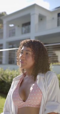 Dikey video: Mayo ve tişörtlü gülümseyen kadın güneşli günün keyfini çıkarıyor. Yaz, güneş, rahatlama, rahatlama, yüzme, açık hava.