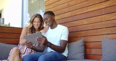 Kanepede oturup tablet kullanan ve birlikte vakit geçirmekten zevk alan farklı çiftler. Teknoloji, mutluluk, rahatlık, yaşam tarzı, kapalı alan, ev