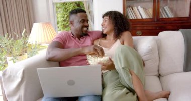 Kanepede dinlenmek, patlamış mısırları paylaşmak ve birlikte dizüstü bilgisayar izlemek. Rahatlama, rahatlama, bağlanma, ev, gündelik, eğlence