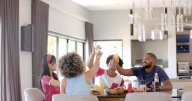 Çeşitli arkadaşlar içkiyle kadeh kaldırıyor, evde yemek masasında birlikte yemek yiyorlar. Kutlama, arkadaşlık, akşam yemeği, sosyalleşme, yeme, parti