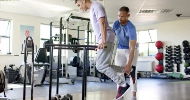 Terapist tarafından desteklenen engelli bir adam rehabilitasyon egzersizi için paralel barlar kullanıyor. Fizyoterapist, fizyoterapi, sağlık, sağlık, iyileşme, terapi, değişmemiş, yavaş çekim