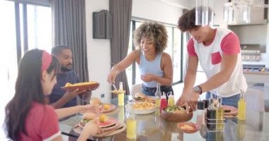 Çeşitli arkadaşlar yemek masasının etrafında yemek ve içecekleri paylaşıyor, birlikte vakit geçiriyorlar. Arkadaşlık, kutlama, toplanma, yemek, parti, birliktelik.