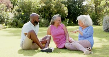 Çimlerin üzerinde oturmuş, üç kıdemli arkadaş parkta sohbet ediyor. Arkadaşlık, boş zaman, açık hava, bağ, doğa, rahatlama.