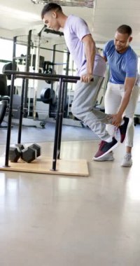 Dikey video: Rehabilitasyondaki adam spor salonunda terapist asistanı ile paralel barlar kullanıyor. fizyoterapi, iyileşme, fizik tedavi, yardım, tıbbi destek, yavaş çekim