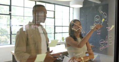 Ofiste iş birliği, meslektaşlar cam tahtaya fikirler yazıp beyin fırtınası yapıyorlar. Takım çalışması, işbirliği, yaratıcılık, tartışma, iş, toplantı