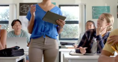 Lisede, genç bir kız sınıfta öğretmen tablet kullanırken elini kaldırıyordu. Eğitim, öğrenci, öğrenme, teknoloji, katılım, ergenlik