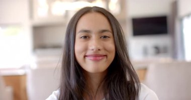 Evde beyaz bluz giyen, gülümseyen melez bir genç kız. Uzun kahverengi saçları, koyu renk gözleri ve açık tenli, değişmemiş, ağır çekimde.