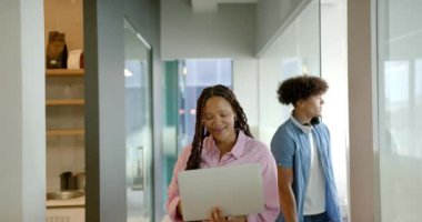 Dizüstü bilgisayar tutan, arka planda iş arkadaşlarıyla ofis koridorunda yürüyen bir kadın. İş, profesyonel, takım çalışması, teknoloji, şirket, işyeri