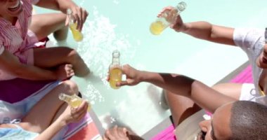 Çeşitli arkadaşlar bira şişeleriyle kadeh kaldırıyor, güneşli bir günde havuz başında eğleniyorlar. Kutlama, yaz, eğlence, eğlence, açık hava