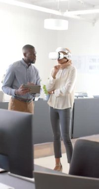 Dikey video: VR kulaklık kullanan kadın, meslektaşı ile iş yerinde tablet tutan projeyi tartışıyor. Teknoloji, işbirliği, takım çalışması, yenilik, sanal gerçeklik, iş