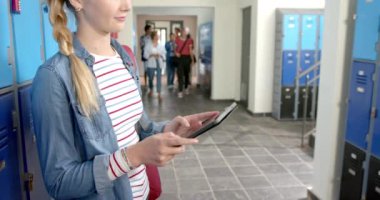 Okul koridorunda dolapların yanında duran tablet kullanan genç bir kız. Eğitim, teknoloji, öğrenci, öğrenme, gençlik, gençlik