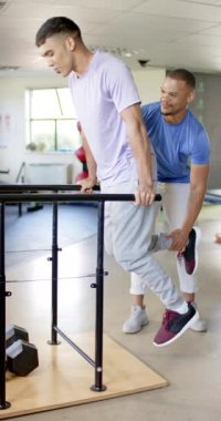 Dikey video: Terapistle paralel barlarda egzersiz yapmak, rehabilitasyon terapisinde engelli bir adam. Fizyoterapi, sağlık, yardım, iyileşme, destek, egzersiz, yavaş çekim