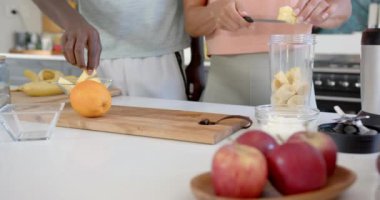 Çeşitli çiftler mutfakta meyve püresi hazırlıyorlar, evde meyve dilimliyorlar. Beyaz kadın sarı saçlı, Afro-Amerikan erkek gri şort giyiyor, değişmemiş, ağır çekimde.