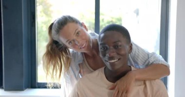 Birbirlerine sarılmış, pencerenin yanında gülümseyen bir çift. Beyaz kadın sarı saçlı, Afro-Amerikan erkek kısa siyah saçlı, değişmemiş, ağır çekimde.