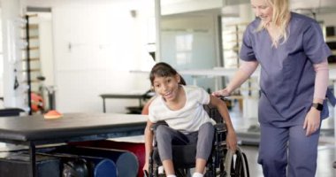 Rehabilitasyon merkezinde terapist, terapi seansı sırasında tekerlekli sandalyede beyin felci geçiren bir kıza yardım ediyor. Fizyoterapi, sağlık, destek, destek, hareket kabiliyeti, bakıcı, değişmemiş, yavaş çekim