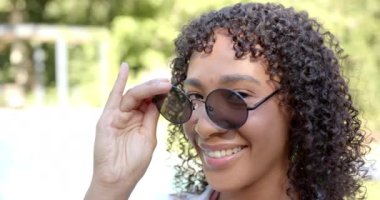 Kıvırcık saçlı gülümseyen kadın açık havuzda güneşli bir günün tadını çıkarıyor. Yaz, rahatlama, tatil, mutluluk, havuz başı