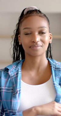 Dikey video: Gülümseyen Afro-Amerikan kadın evde, kameraya bakıyor. Portre, mutluluk, günlük kıyafet, yaşam tarzı, iç mekan, özgüven, yavaş çekim