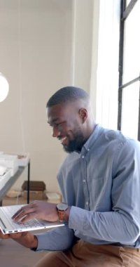 Dikey video: Ofiste otururken dizüstü bilgisayarda yazan gülümseyen işadamı. profesyonel, kurumsal, girişimci, teknoloji, işyeri, üretkenlik