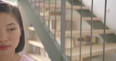 Modern evdeki kitaplıklarla merdivenlerin yanında gülümseyen Asyalı kadın. iç mekan, mutluluk, yaşam tarzı, kitaplık, çağdaş, rahatlama