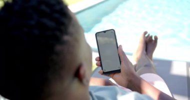 Havuzda dinlenmek, sandalyede uzanırken akıllı telefon kullanmak, fotokopi çekmek. Rahatlama, yaz, eğlence, teknoloji, açık hava, tatil