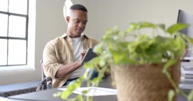Tablet kullanan, tekerlekli sandalyede oturan, modern ofis ortamında çalışan bir adam. Teknoloji, erişilebilirlik, ticaret, çalışma alanı, üretkenlik, profesyonellik